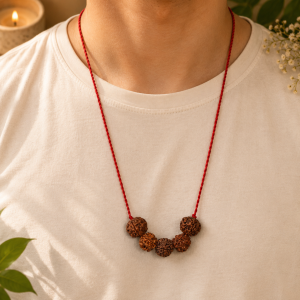 Red cord necklace with five carved wooden beads resting on a white shirt warm ambient light in the background